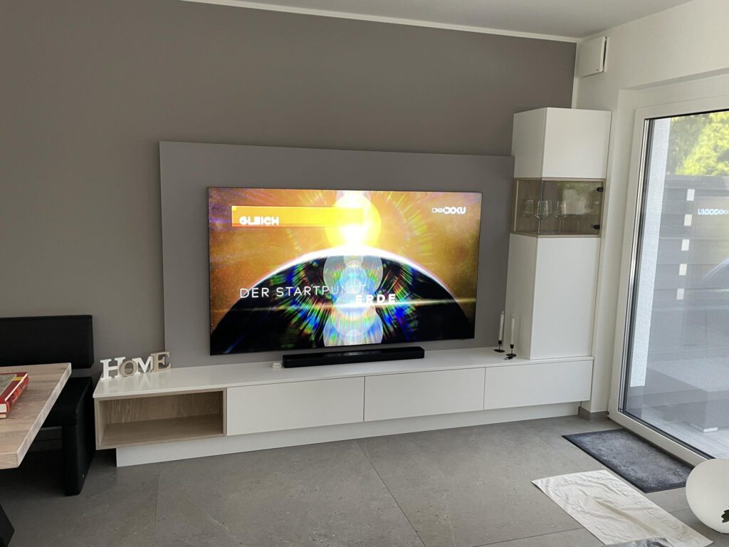 Moderne Wohnwand mit TV-Lowboard in Weiß und Holz-Akzenten – Maßanfertigung der Schreinerei Pass-Genau in Pulheim.