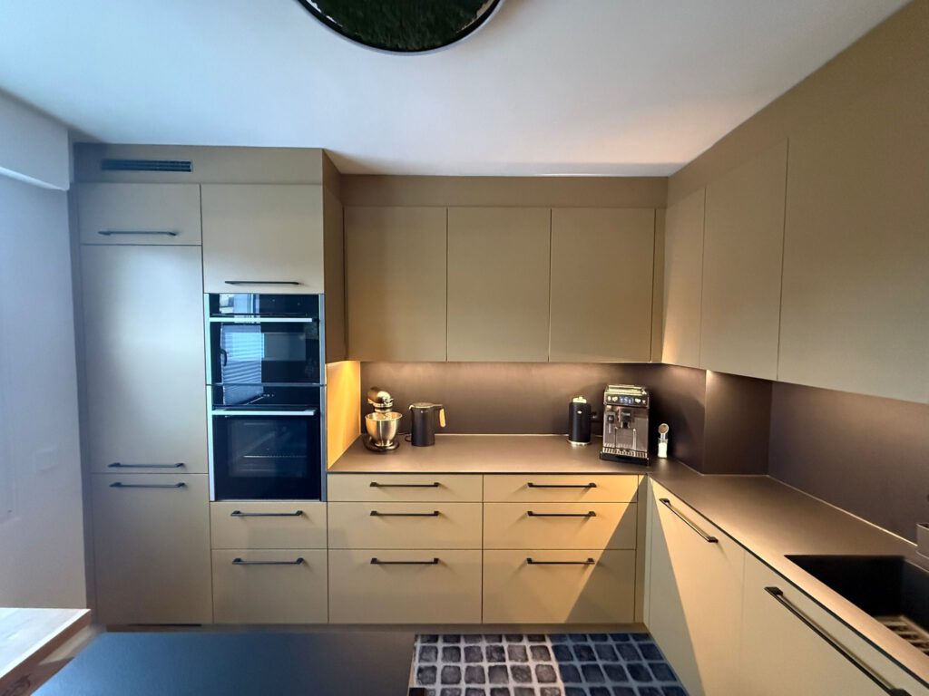 L-förmige Einbauküche in edlem Sandton mit dunkler Arbeitsplatte und stimmungsvoller Unterbau-Beleuchtung.