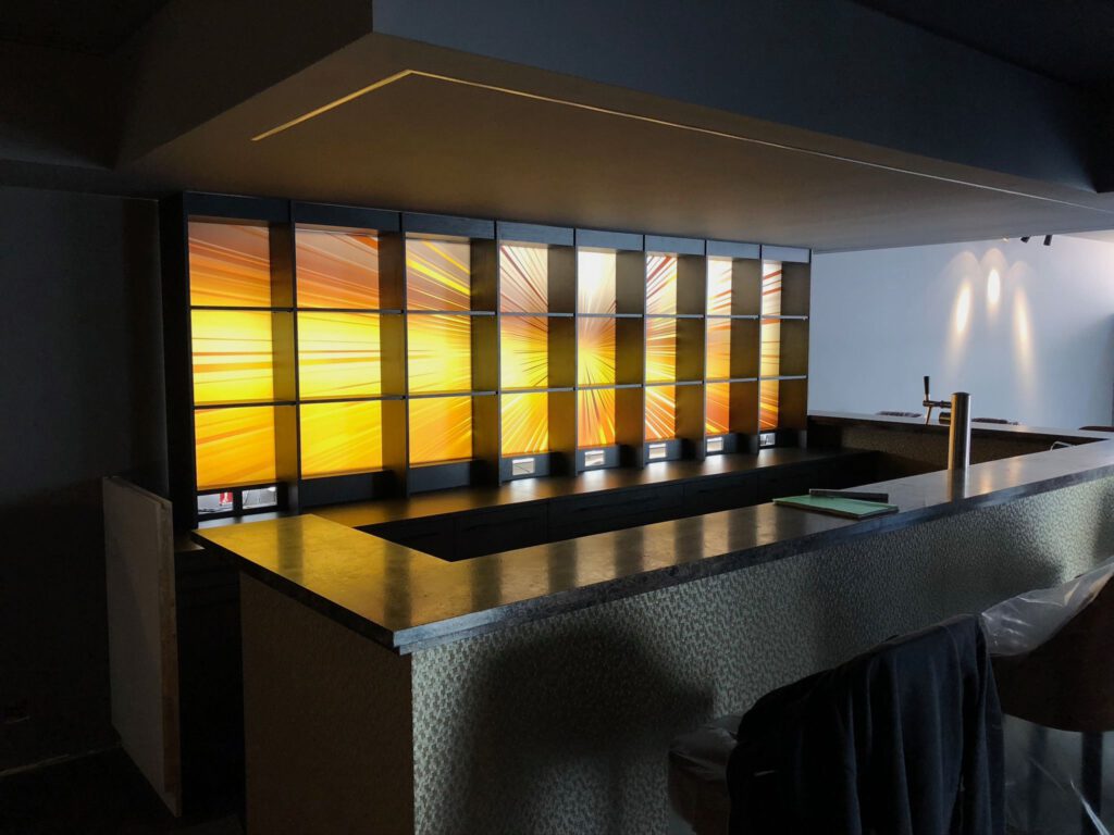 Moderne Bartheke mit hinterleuchtetem Regal in gelb-orangefarbener Strahlenoptik von Schreinerei Pass-genau.