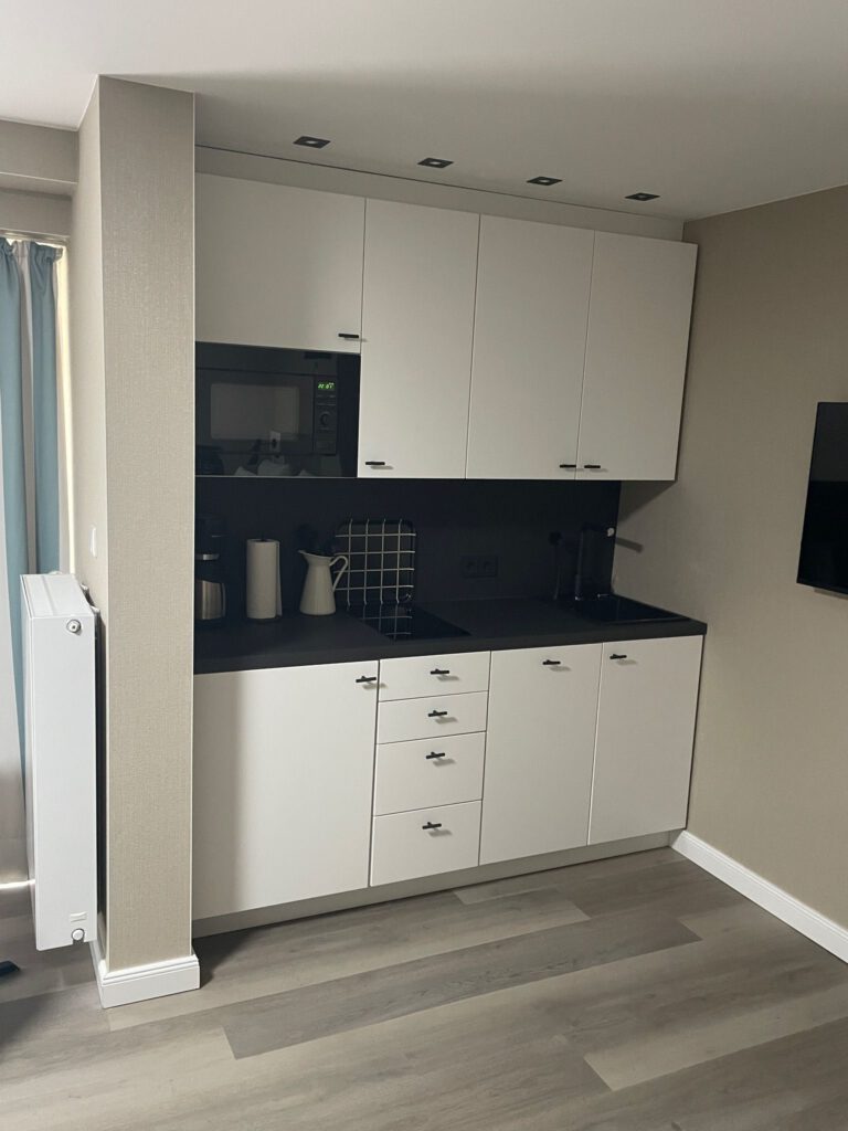 Kleine, weiße Kompaktküche mit schwarzen Griffen und dunkler Rückwand, ideal für Apartments oder Büros.
