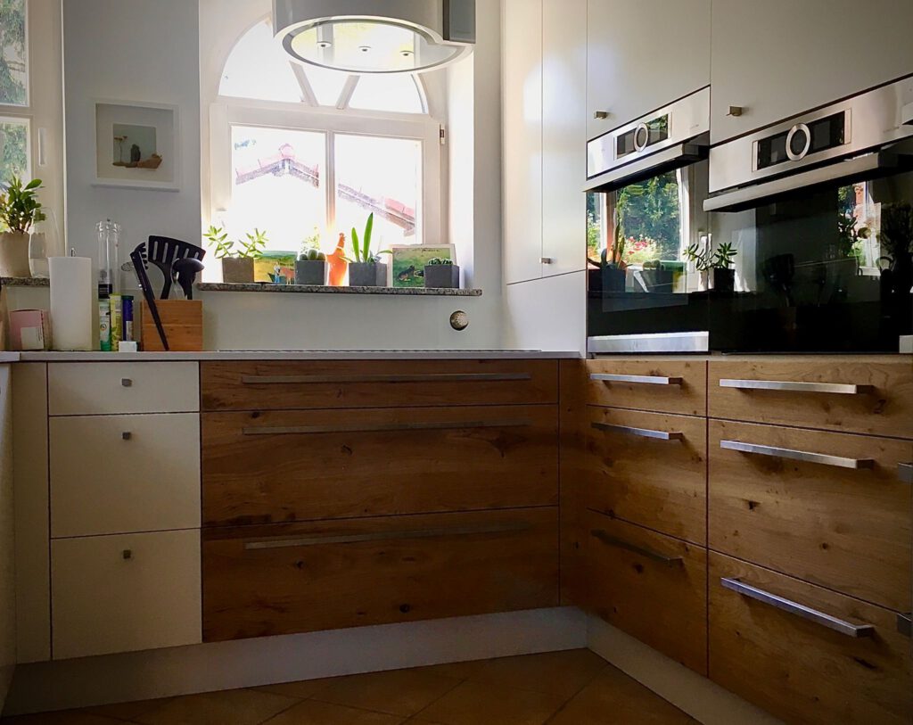 Detailaufnahme von Küchenunterschränken aus Massivholz mit langen Edelstahlgriffen und präziser Kantenführung.