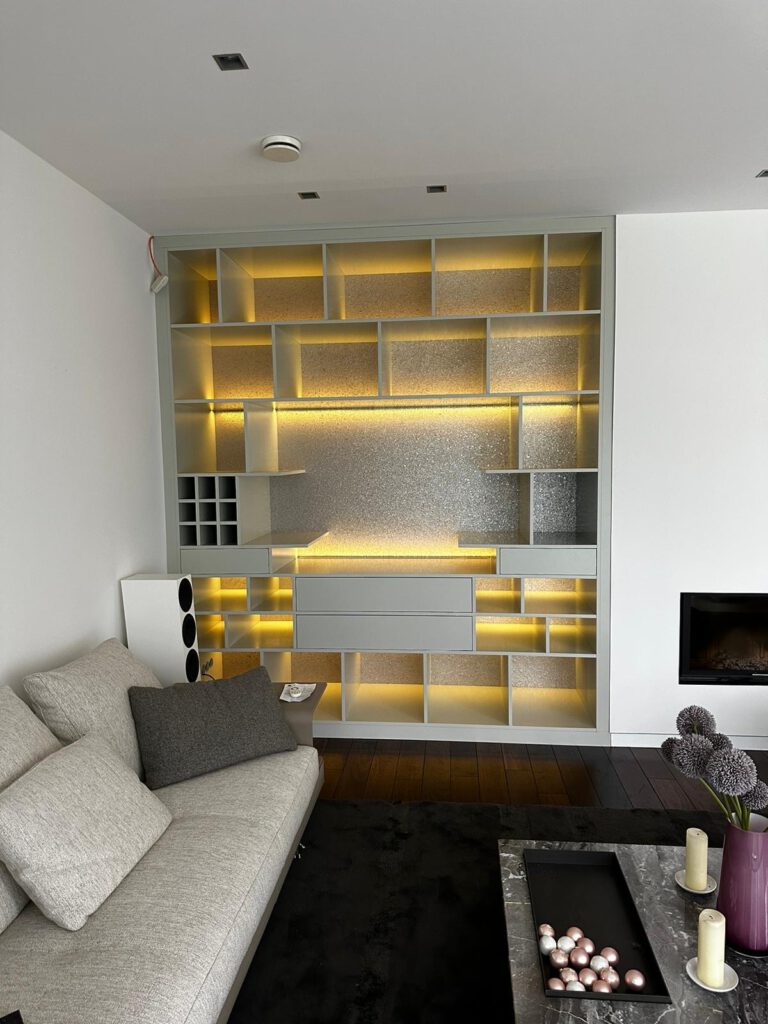 Frontalansicht eines deckenhohen Einbauregals mit indirekter LED-Beleuchtung und strukturierter Rückwand von Schreinerei Pass-genau.